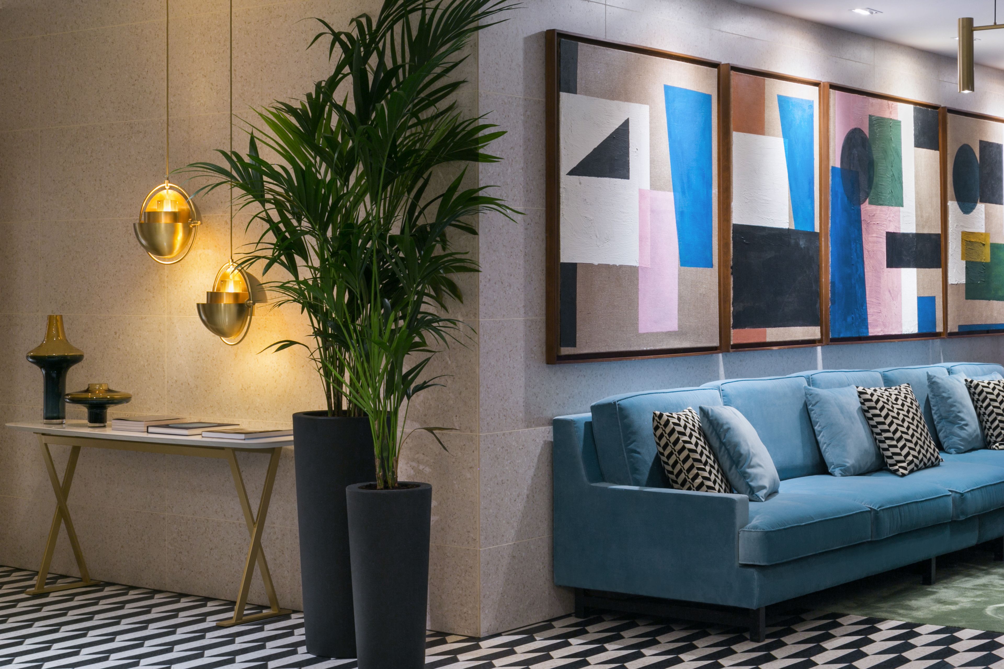 A modern lobby with a blue sofa, a large abstract painting, and a potted plant.