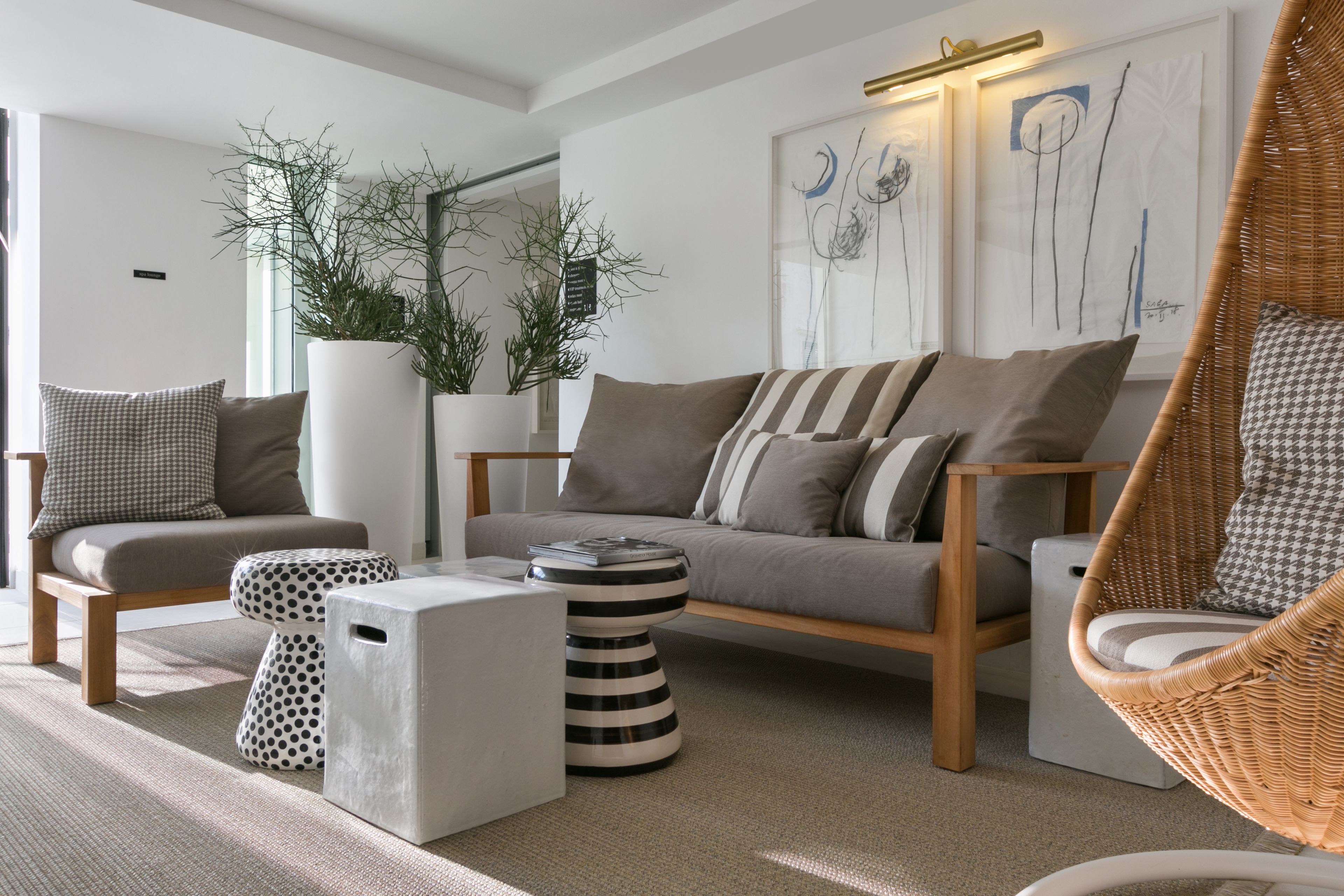 Una sala de estar moderna con sofá, sillones, una mesa de centro y una silla colgante. Hay plantas en macetas y obras de arte en las paredes.