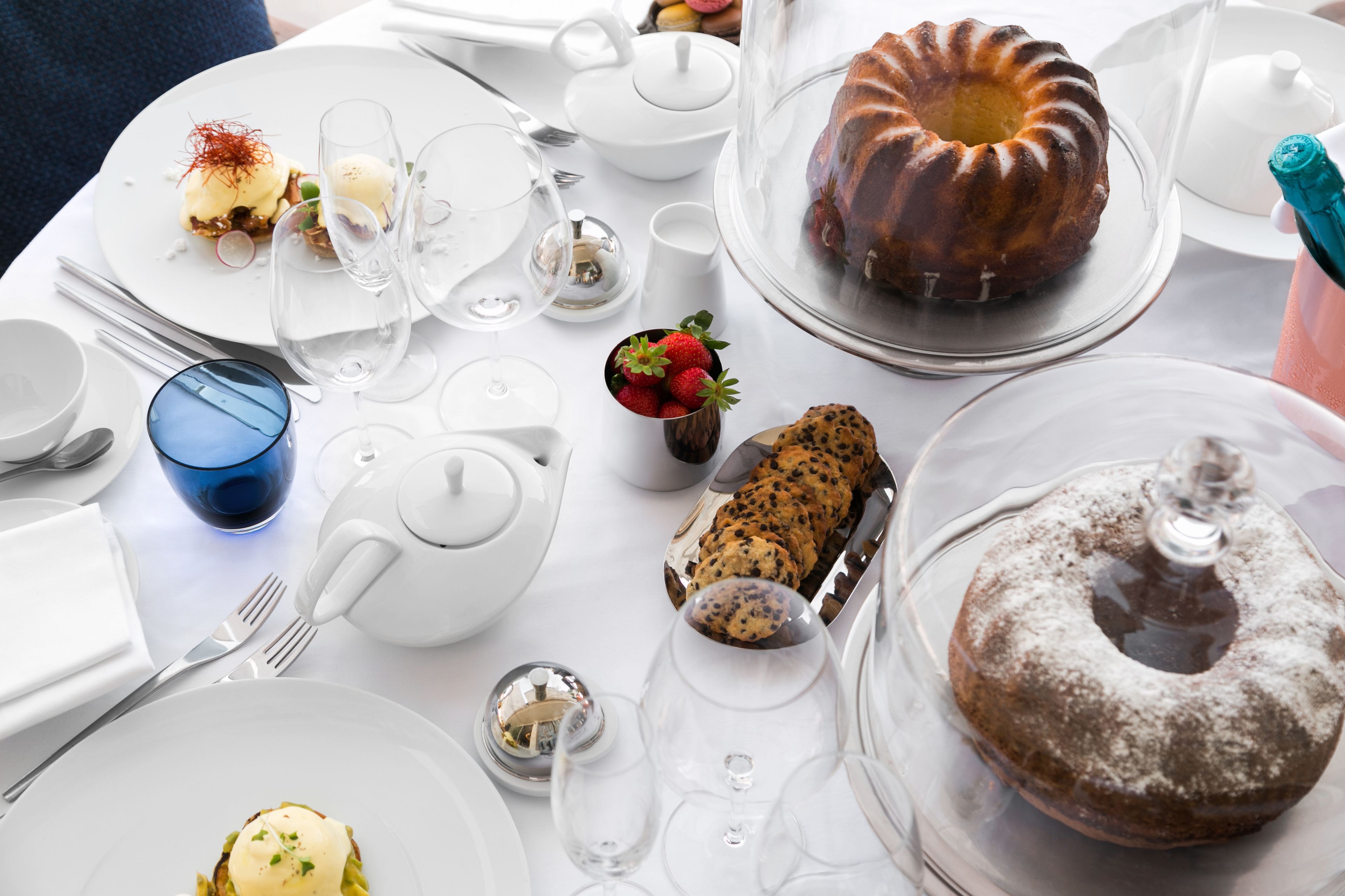 A table set with various dishes, including a bundt cake, a chocolate dessert, and a fruit arrangement.