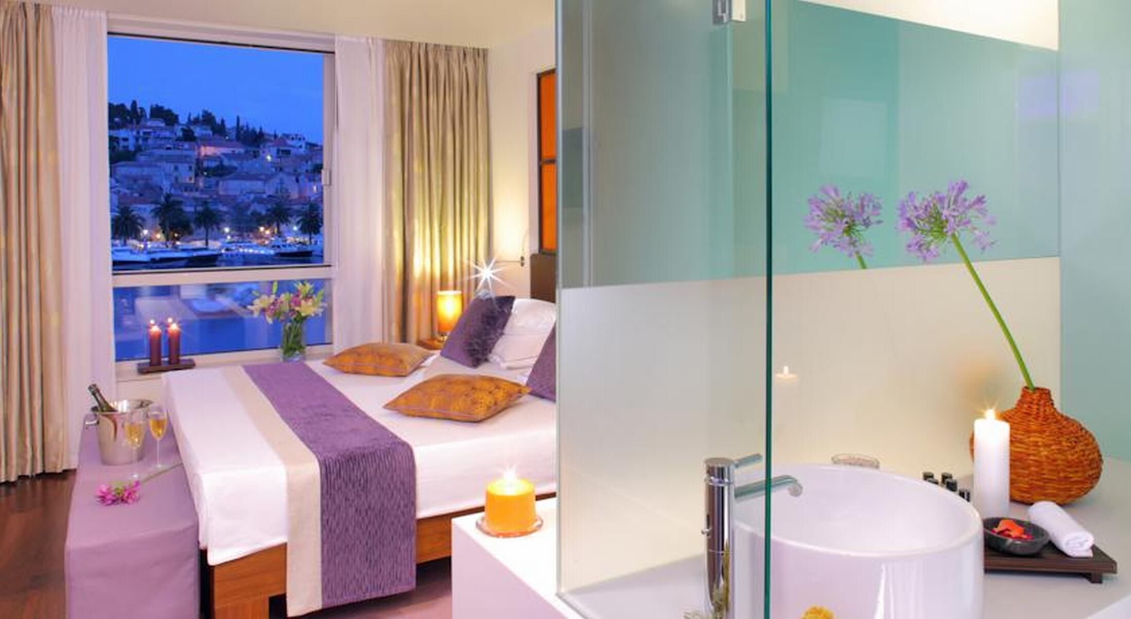 Habitación de hotel con cama, ventana con vista a la ciudad, baño con bañera y espejo.