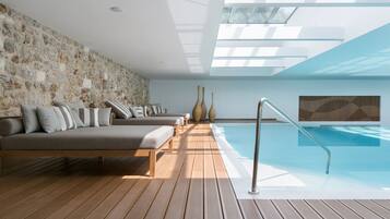A modern indoor pool area with a stone wall, wooden deck, and a large window.