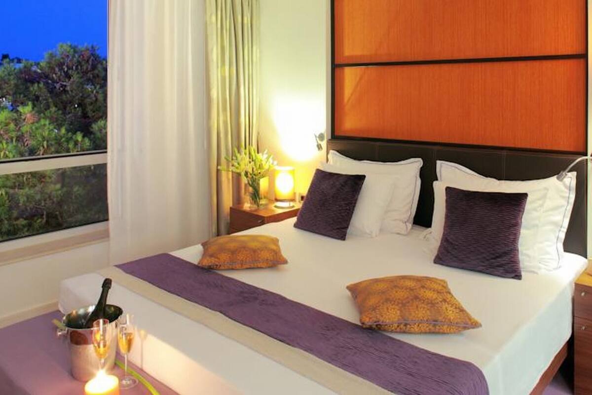 A hotel room with a bed, a nightstand, a window with a view, and a bedside table with a candle.