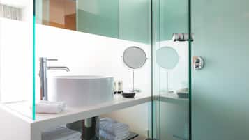 Un baño moderno con un lavamanos grande de color blanco, un espejo redondo y cabina de ducha de vidrio.