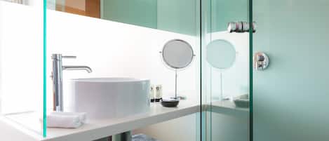 Une salle de bain moderne avec un grand lavabo blanc, un miroir rond et une cabine de douche en verre.