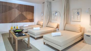 A modern hotel room with two sofas, a small wooden table with a fruit bowl, and a large abstract wooden panel on the wall.