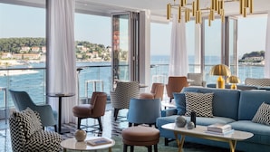 A modern living room with a view of the sea, featuring a blue sofa, patterned chairs, and gold pendant lights. - Adriana Hvar Spa Hotel (Hvar)