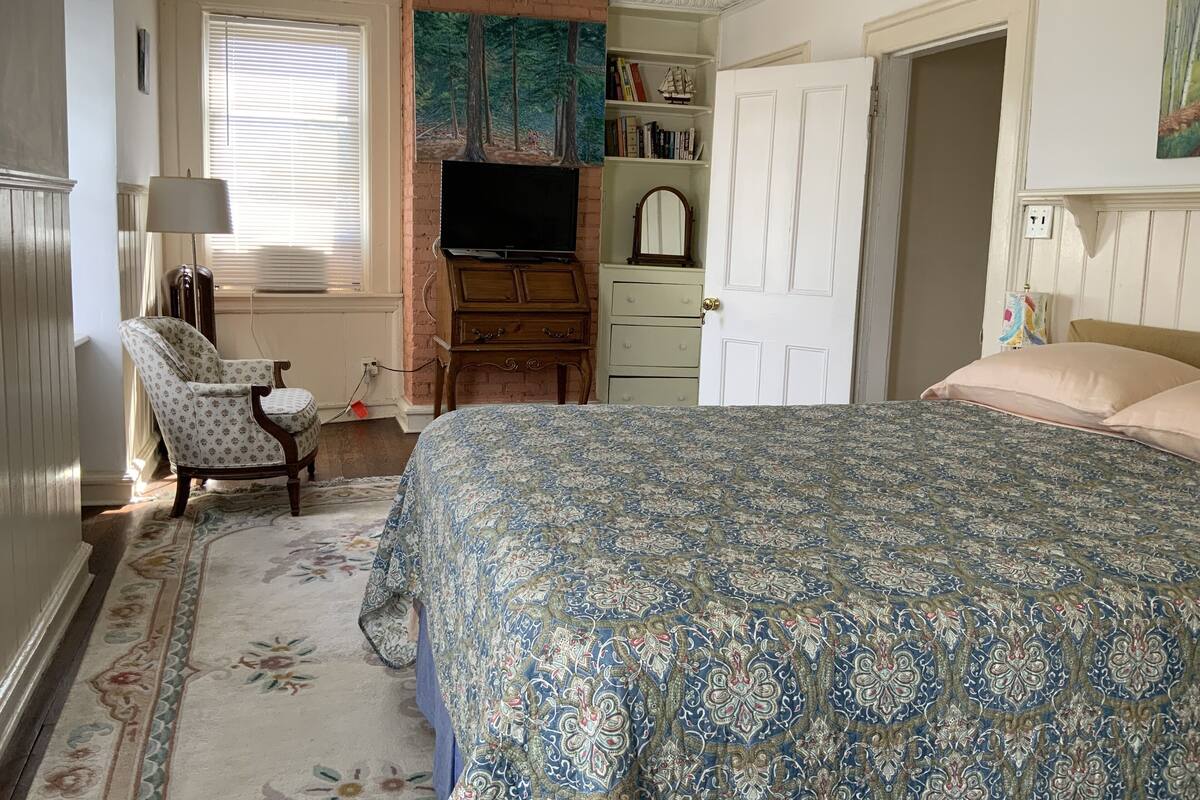 A bedroom with a large bed, a chair, a dresser, a television, and a door.