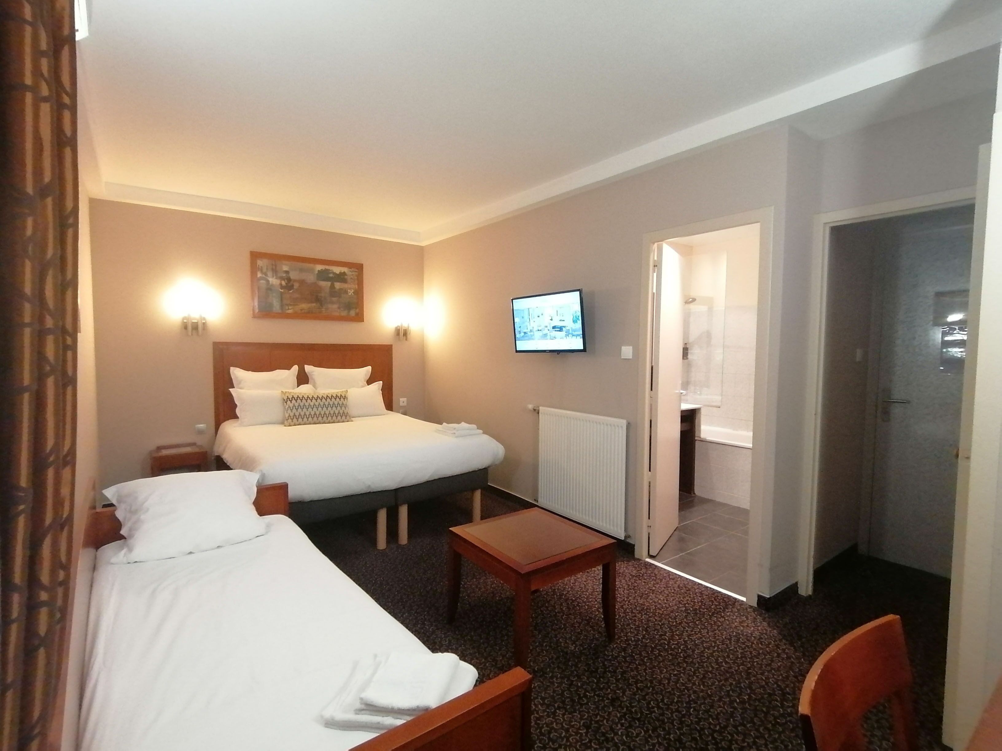 A hotel room with two beds, a TV, a small table, and a chair.