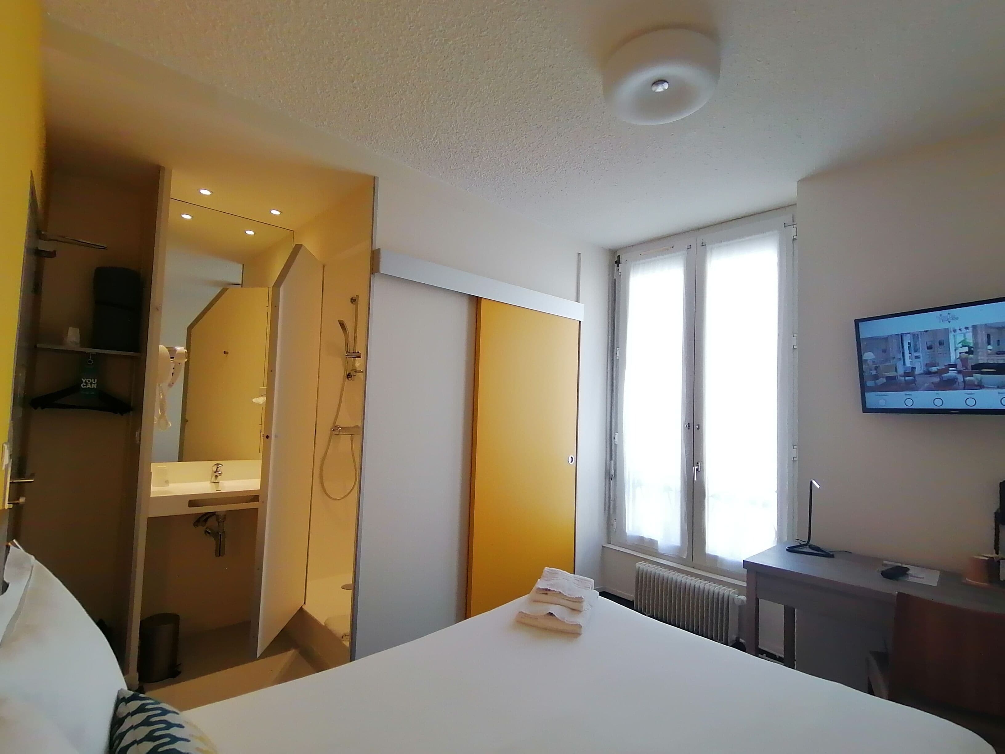 A hotel room with a bed, a desk, a television, a window, and a bathroom with a shower.