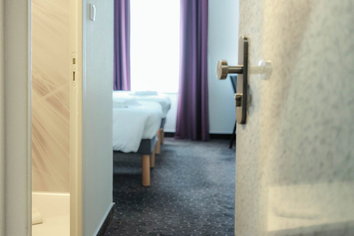 A hotel room with a bed, a desk, and a window with curtains.