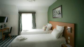 A hotel room with two beds, a desk, a TV, and a window with curtains.