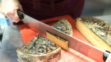 A person slicing a large wheel of cheese on a metal surface.