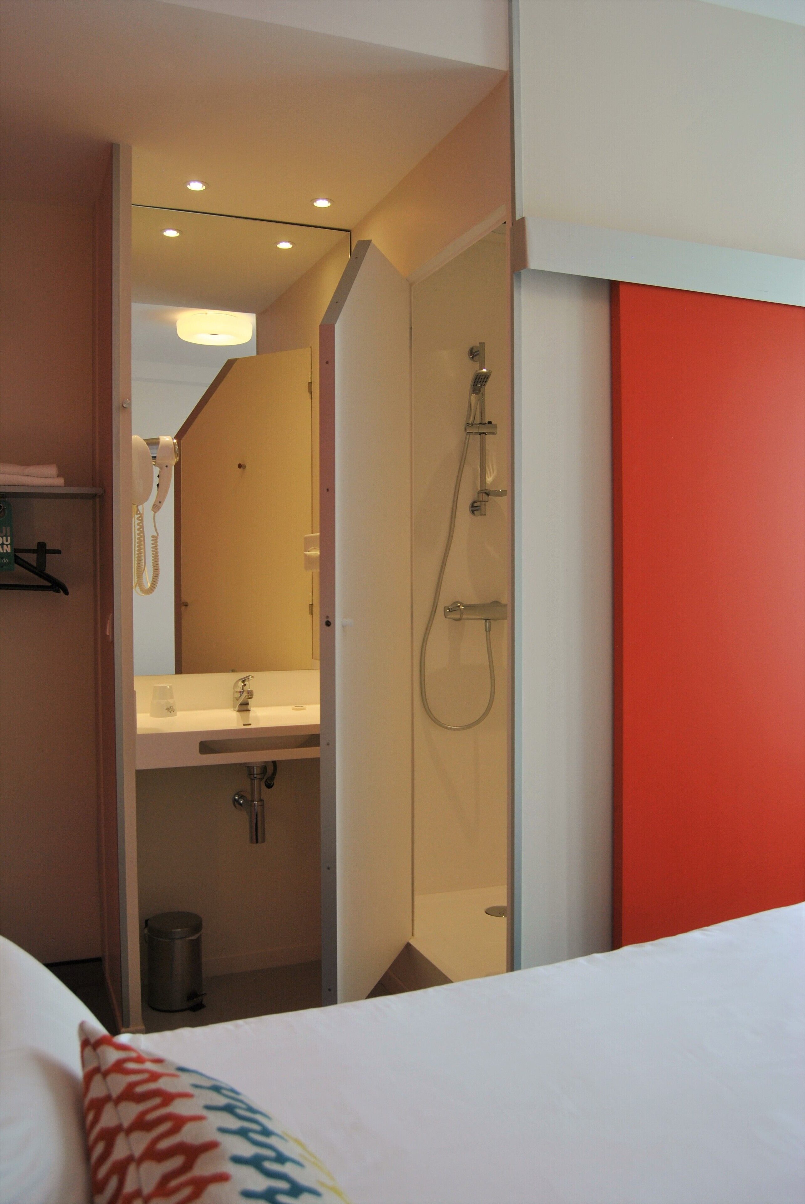 A hotel room with a bed, a bathroom with a shower, a sink, and a trash can.