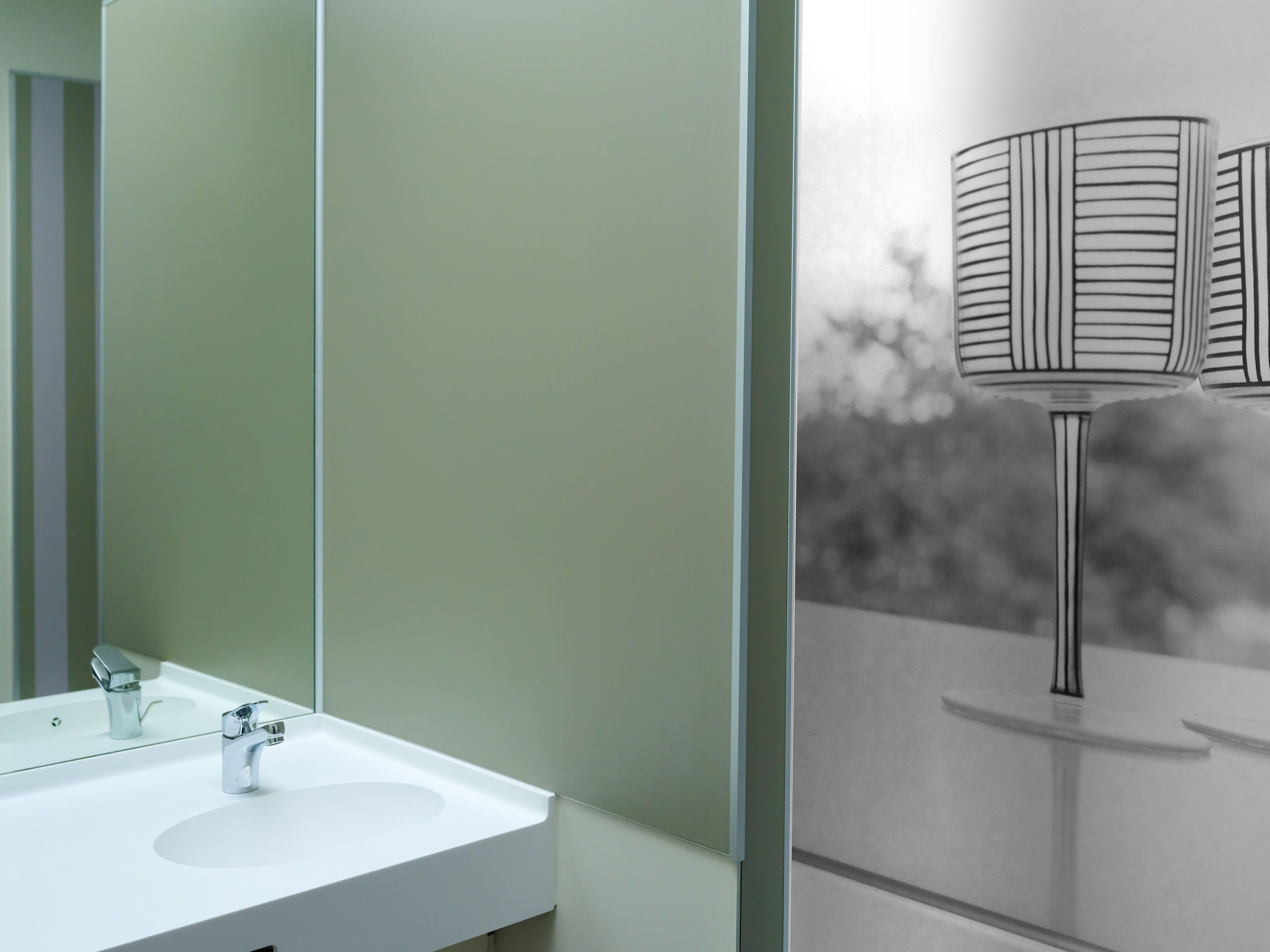 Ein Badezimmer mit weißem Waschbecken, einem Spiegel und einer Wandlampe.