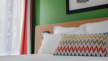 Una habitación de hotel con una cama, un almohadón de estampado geométrico y un cuadro enmarcado en la pared.