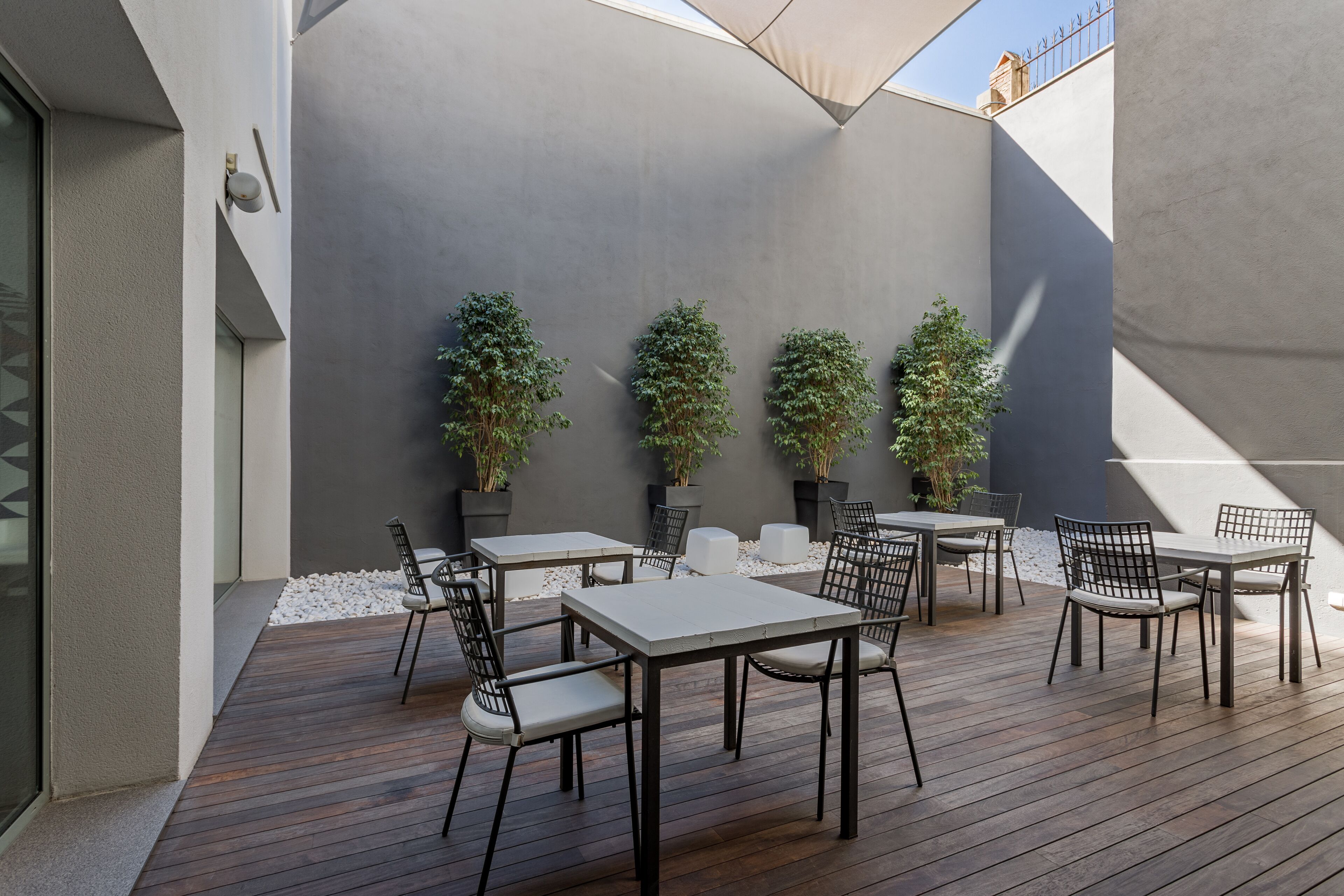 An outdoor patio with wooden flooring, tables, and chairs. There are potted plants and a large umbrella providing shade.