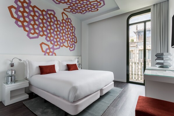 A modern hotel room with a large bed, a glass desk, and a balcony with a view of the city. - Room Mate Carla, Barcelona (Barcelona)