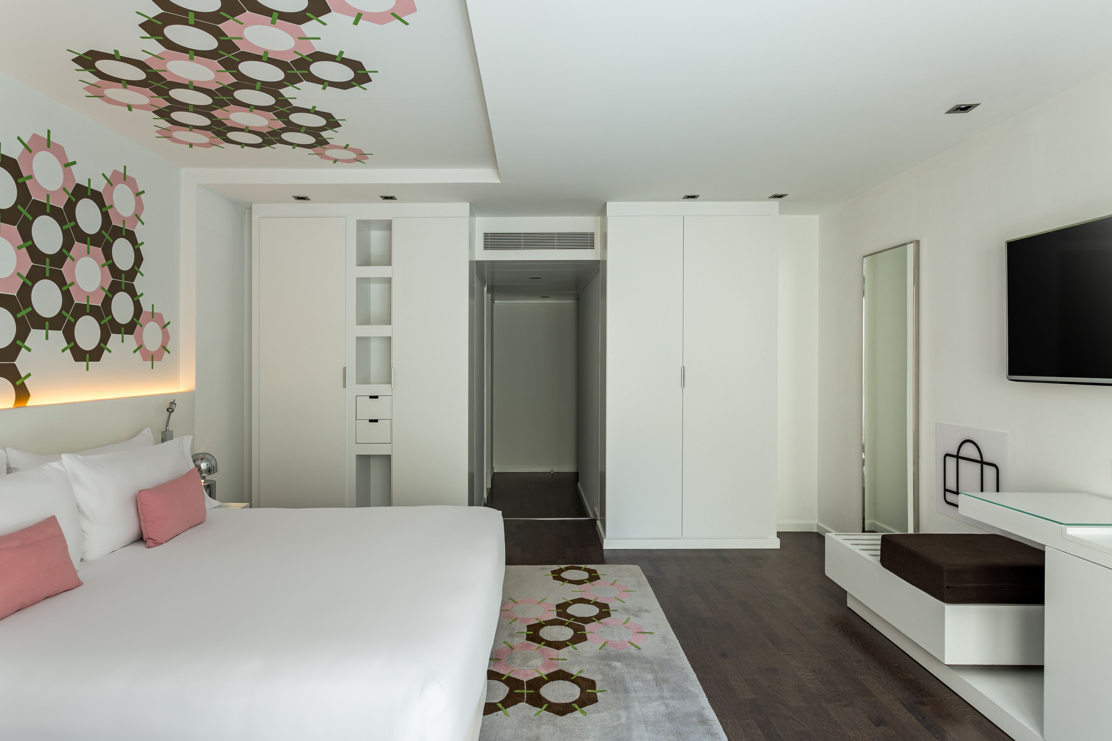 Una habitación de hotel moderna con una cama grande, un vestidor amplio, un escritorio de vidrio y un televisor de pantalla plana.