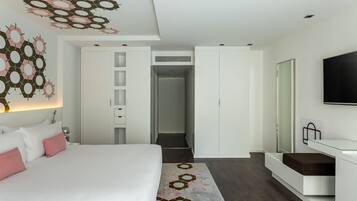 Una habitación de hotel moderna con una cama grande, un vestidor amplio, un escritorio de vidrio y un televisor de pantalla plana.
