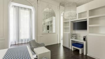 Een moderne hotelkamer met een groot bed, een zithoek met gestreepe banken, een televisie op een witte standaard en een groot, rondbogig raam met gordijnen.