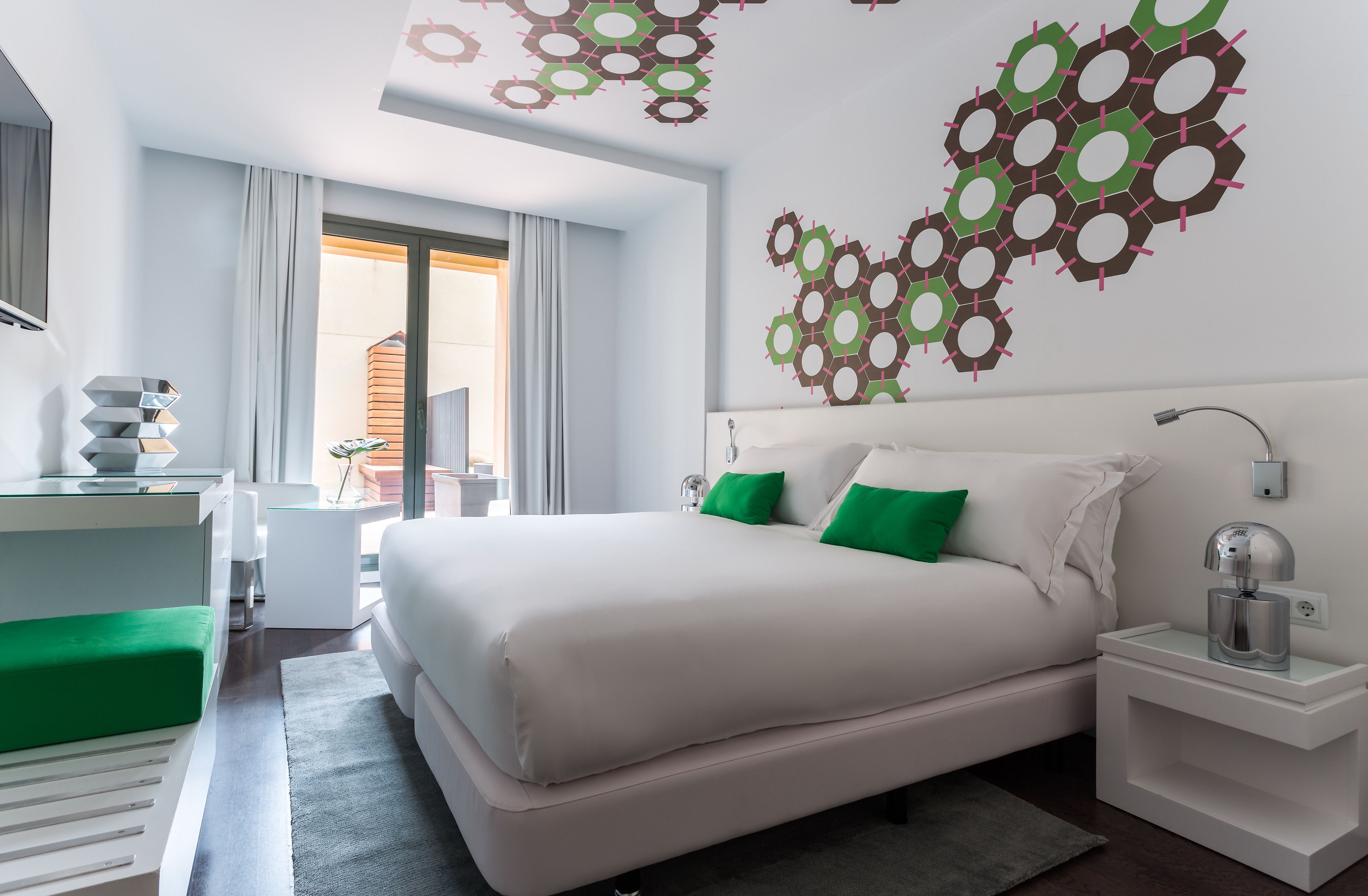 A modern hotel room with a large bed, a desk, and a view of the outdoors.