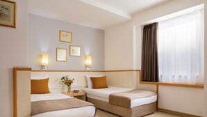 Habitació d'hotel amb dos llits, una cambrera de nit amb una làmpada, quadres a la paret i una finestra amb cortines.
