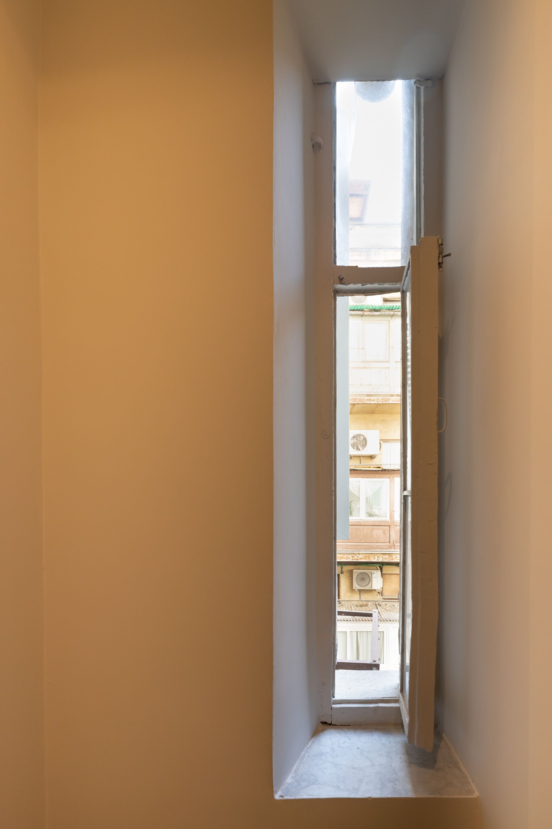 Ein schmaler Flur mit einem kleinen Fenster, das auf einen Balkon im Freien führt.