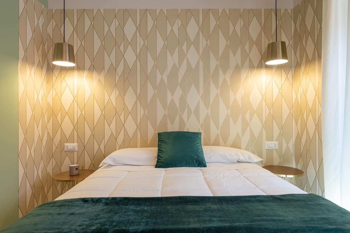 Ein ordentlich bezogenes Bett mit einem grünen Kissen, zwei Nachttischen und einer Wand mit geometrischem Muster.