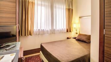 A hotel room with a bed, a TV, a desk with a remote control, and curtains.