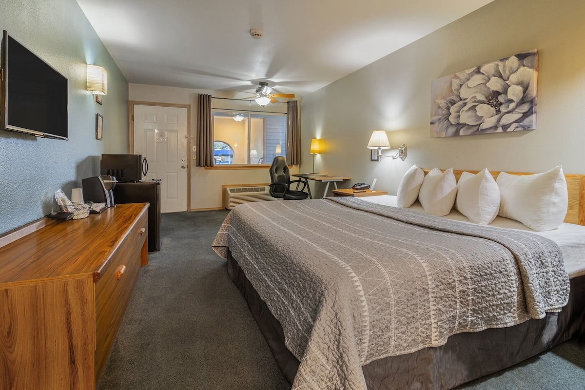 A hotel room with a bed, desk, chair, television, and a ceiling fan.