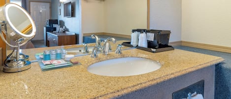 A hotel bathroom with a granite countertop sink, a mirror, toiletries, and a towel rack.