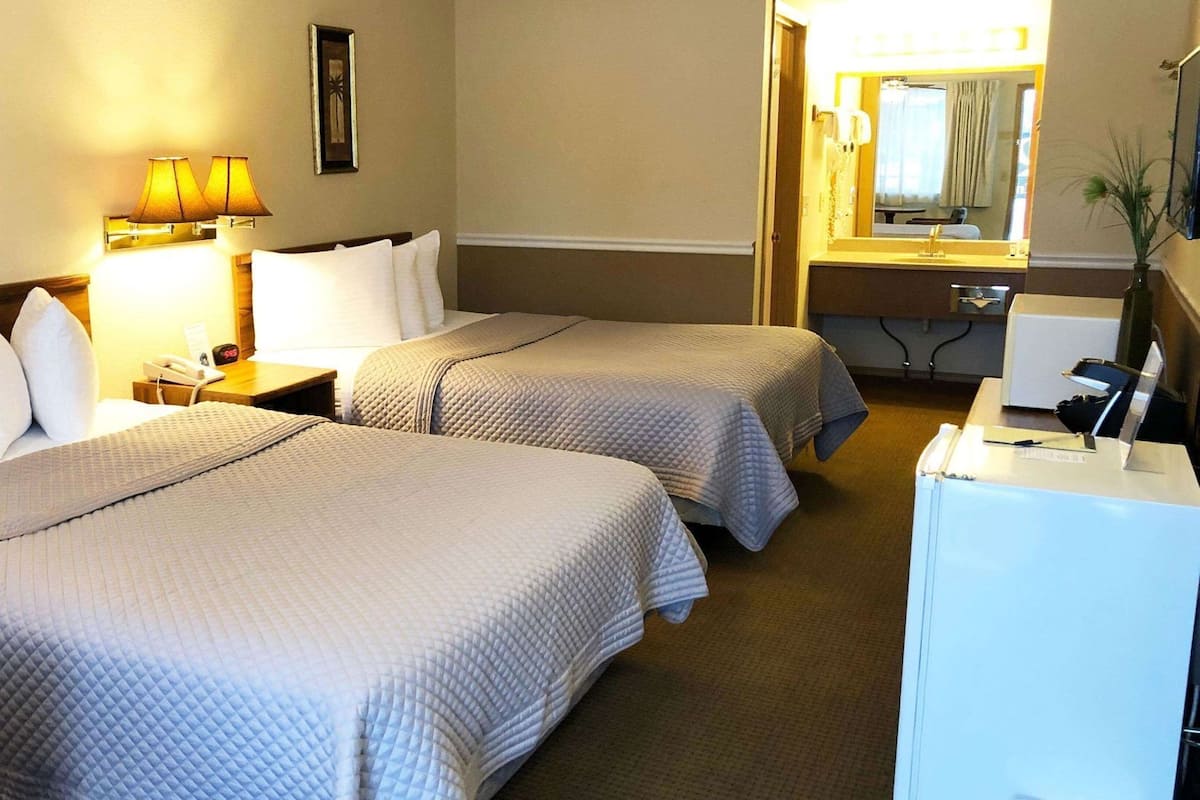 A hotel room with two beds, a desk, a mirror, and a telephone.