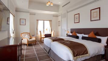 A hotel room with two beds, a desk, a chair, and a large window.