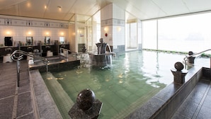 A large indoor swimming pool with multiple water features, a seating area, and a view of the city through large windows.