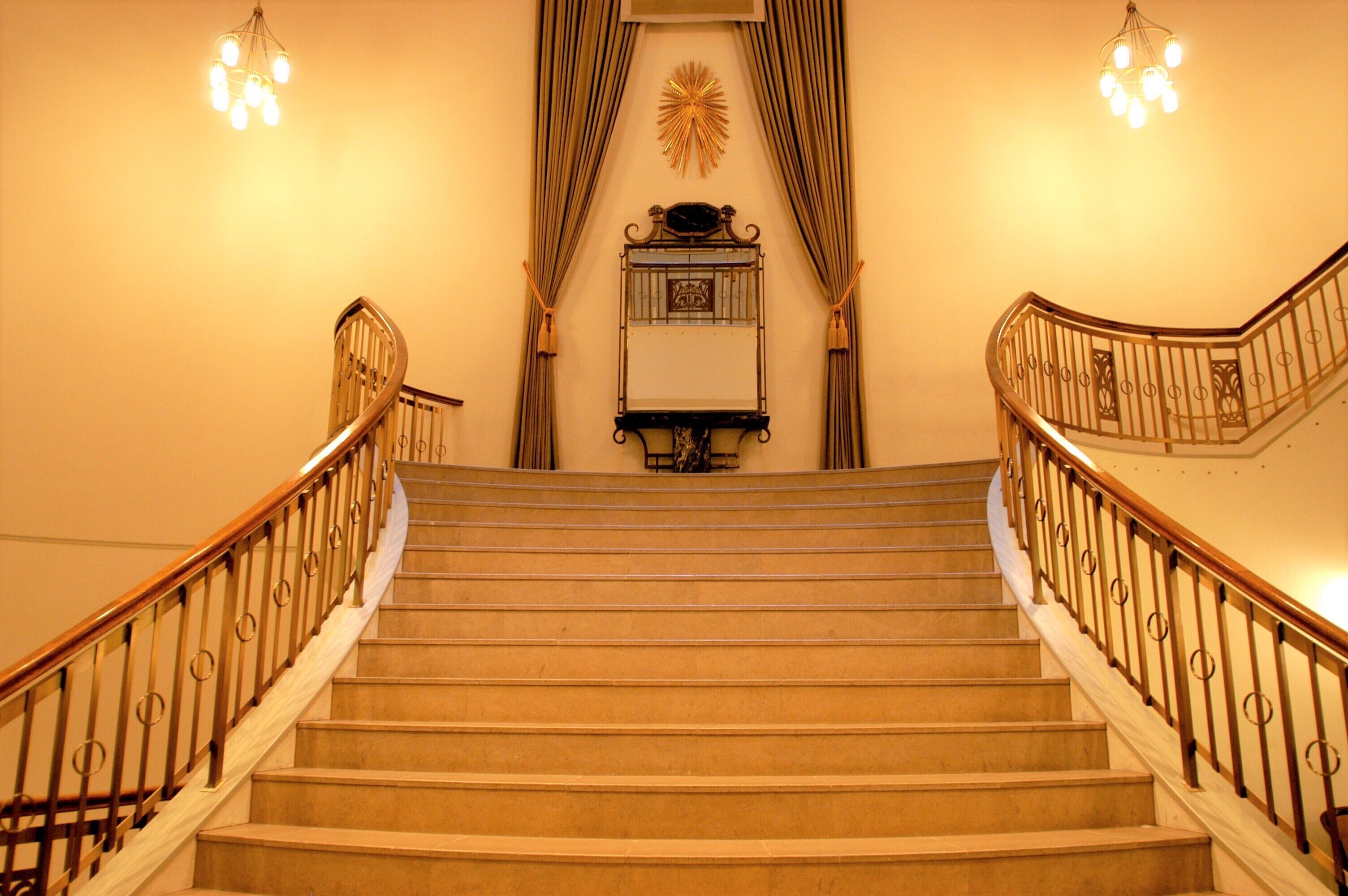 A grand staircase with a curved railing, a decorative wall piece, and a chandelier.