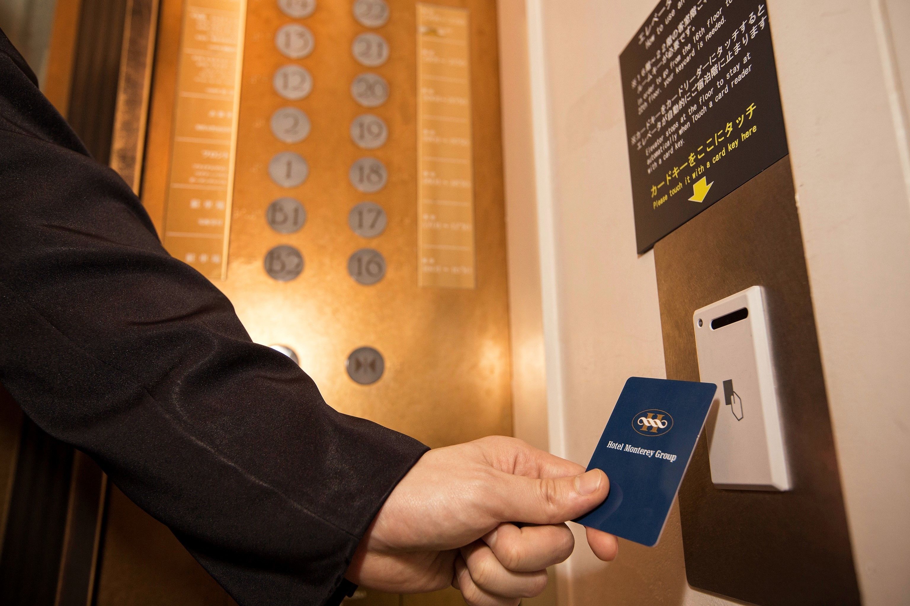 A person holding a card near an elevator control panel with a sign indicating a card reader.