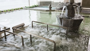 An indoor swimming pool with a water fountain, metal handrails, and a view of the city through large windows.
