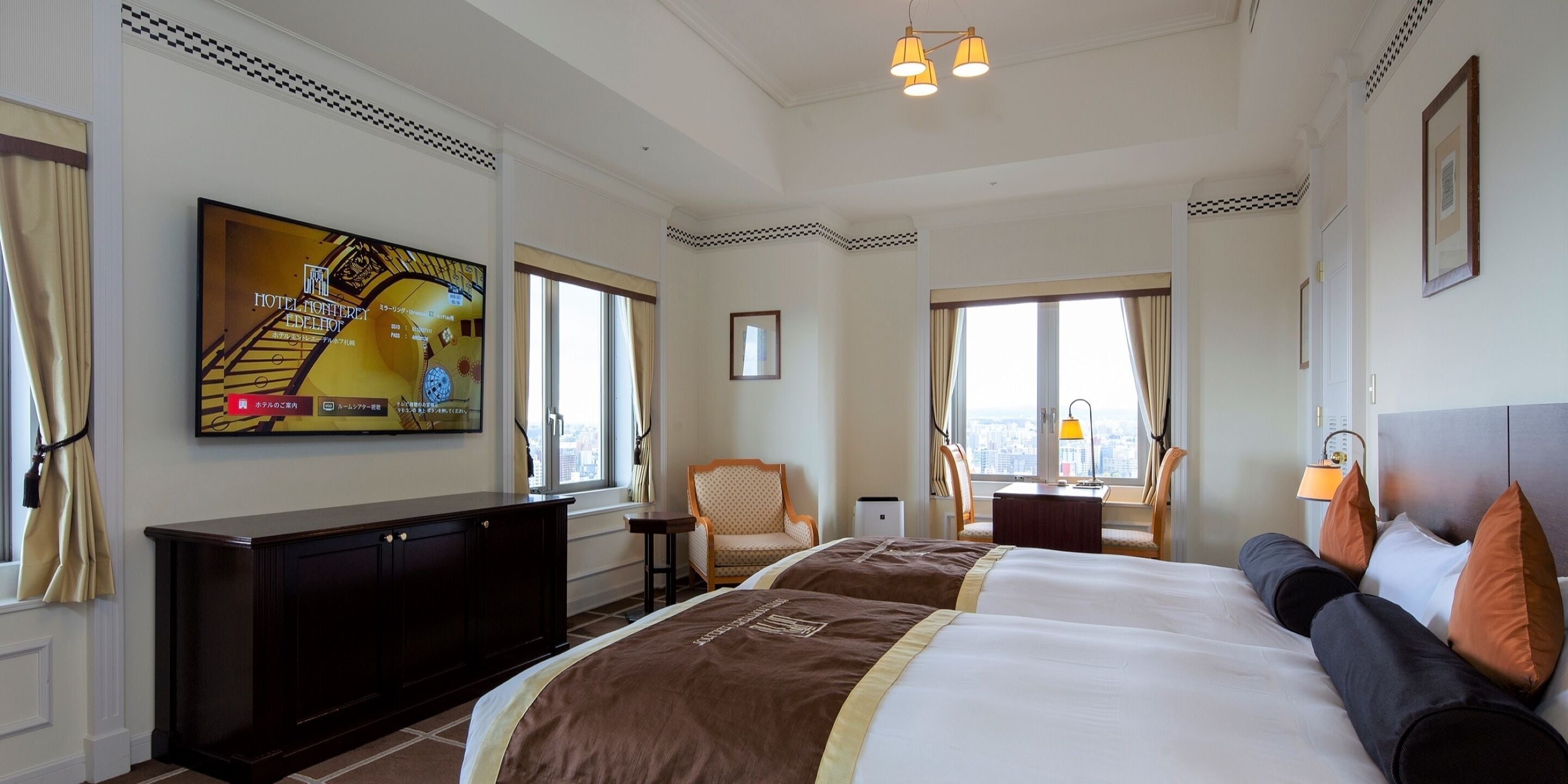 A hotel room with a large bed, a TV mounted on the wall, a desk, and a chair.