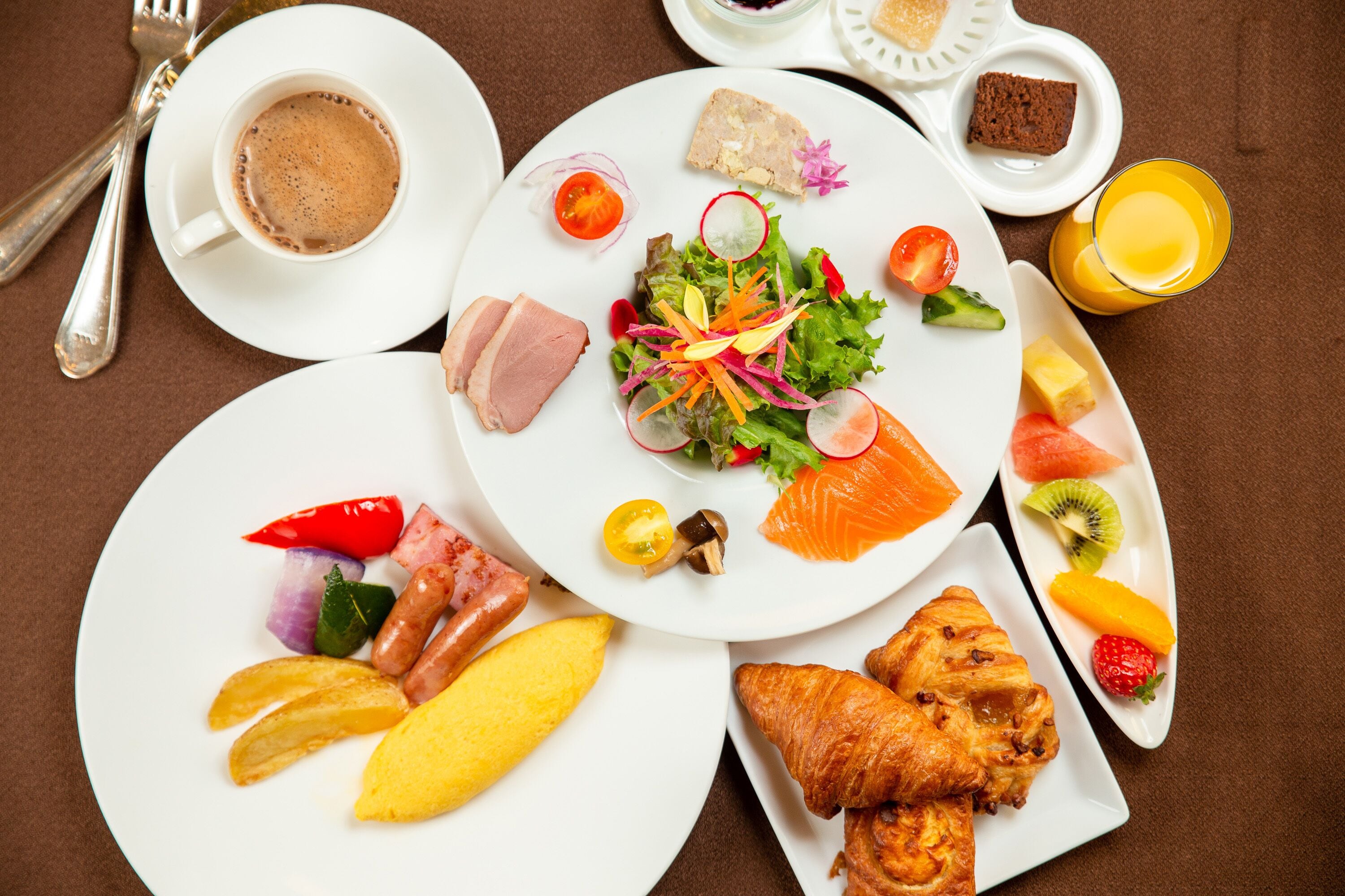 A breakfast setting with plates of food, including eggs, ham, croissants, and a salad.