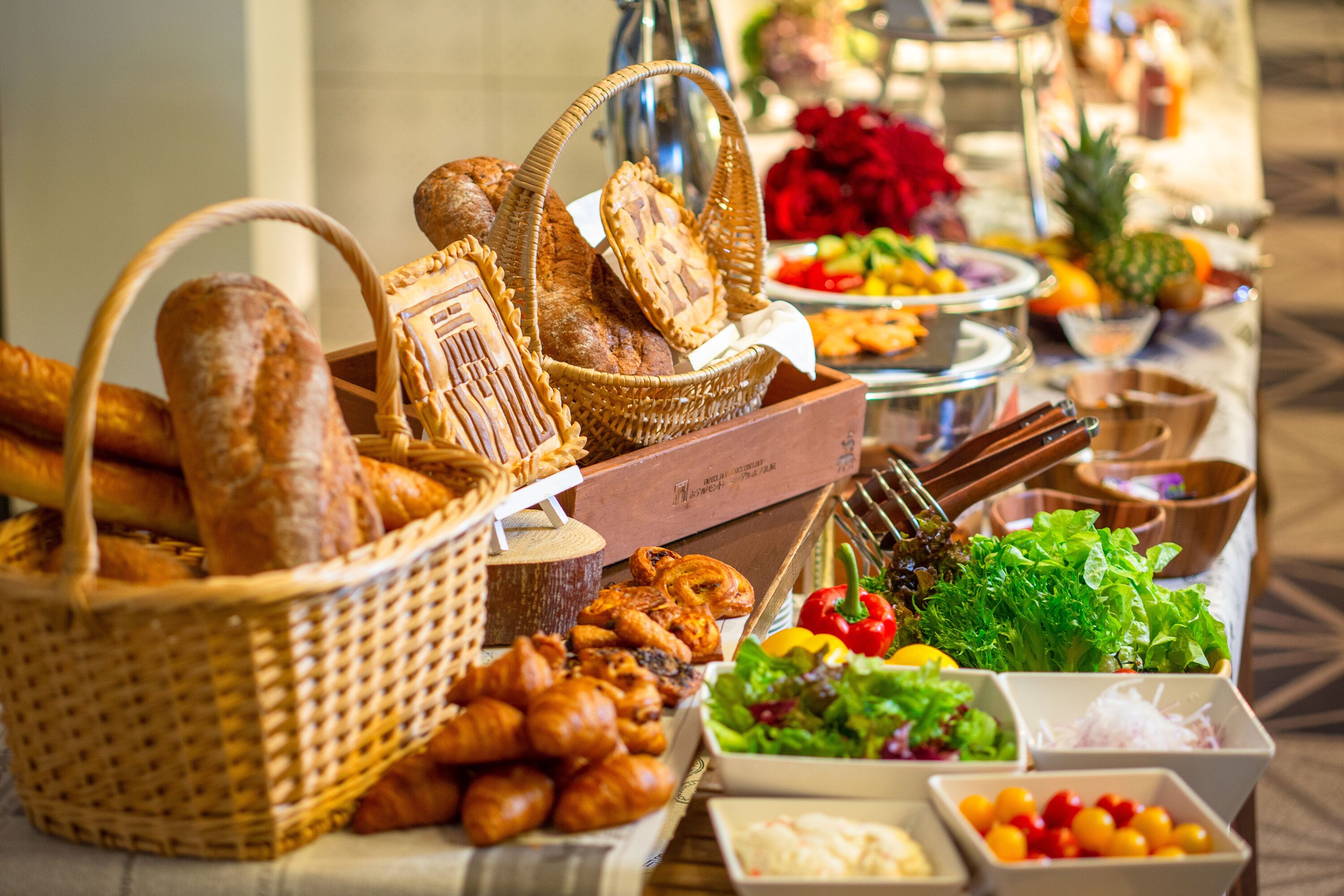 A buffet table with various food items including bread, pastries, salads, and fruits.