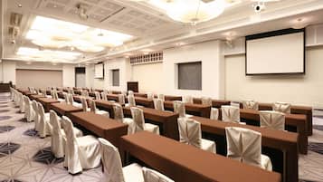 A conference room with rows of tables and chairs, a projector screen, and a patterned carpet.