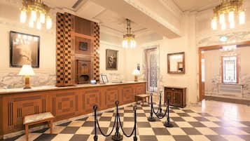 A lobby with a checkered floor, wooden reception desk, and chandeliers.
