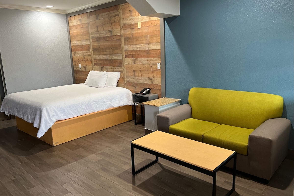A hotel room with a bed, a small table, a chair, and a nightstand with a phone.