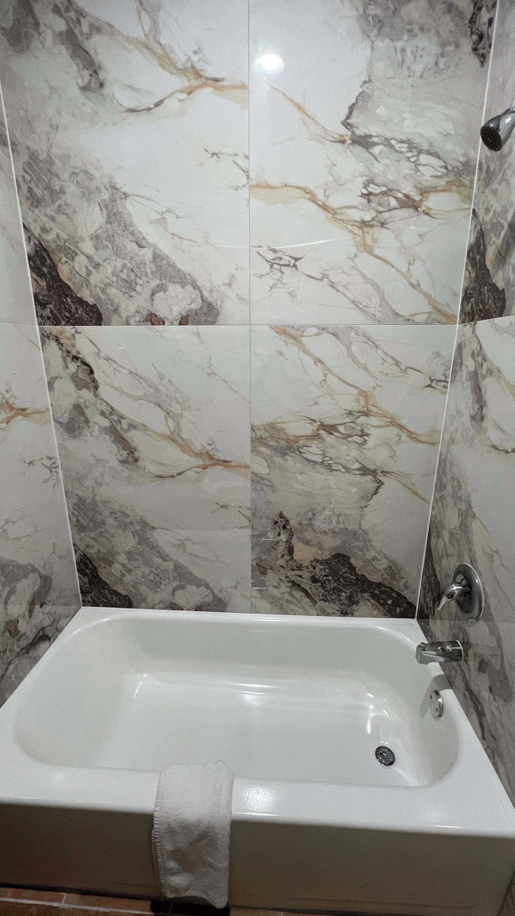 A bathroom with a bathtub, marble walls, and a towel on the tub.