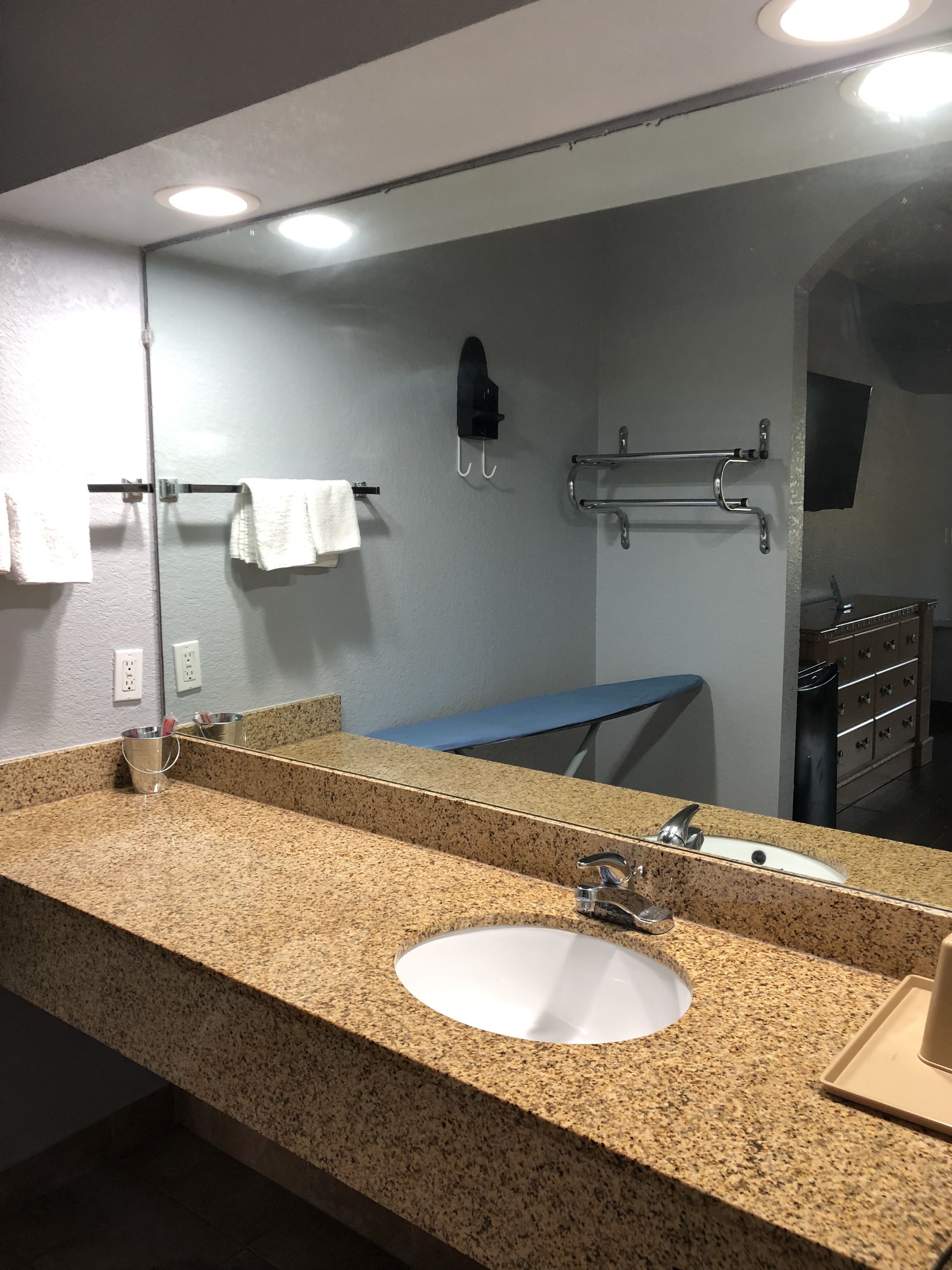 A bathroom with a granite countertop, a white sink, a mirror, a towel rack, and a towel hanging on it.