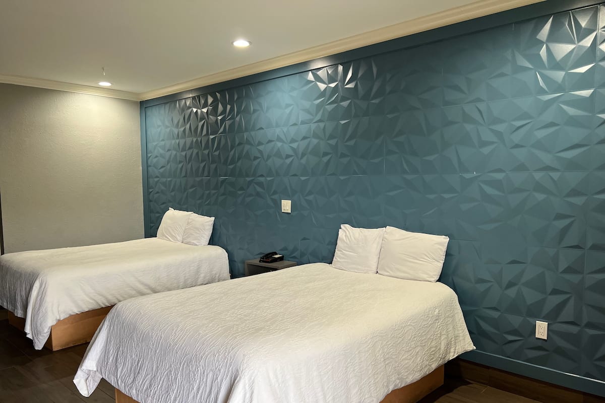 A hotel room with two beds, each with white bedding, a wooden floor, and a blue textured wall.