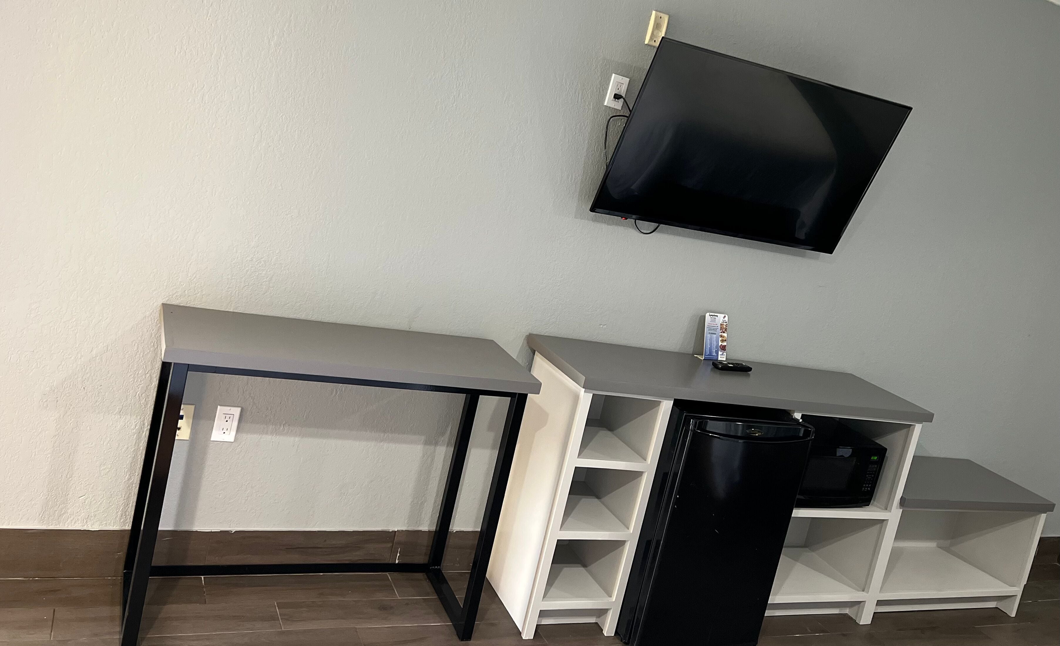 Una habitación con un escritorio, un cesto de basura negro y una televisión montada.