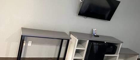A room with a desk, a black trash bin, and a mounted TV.