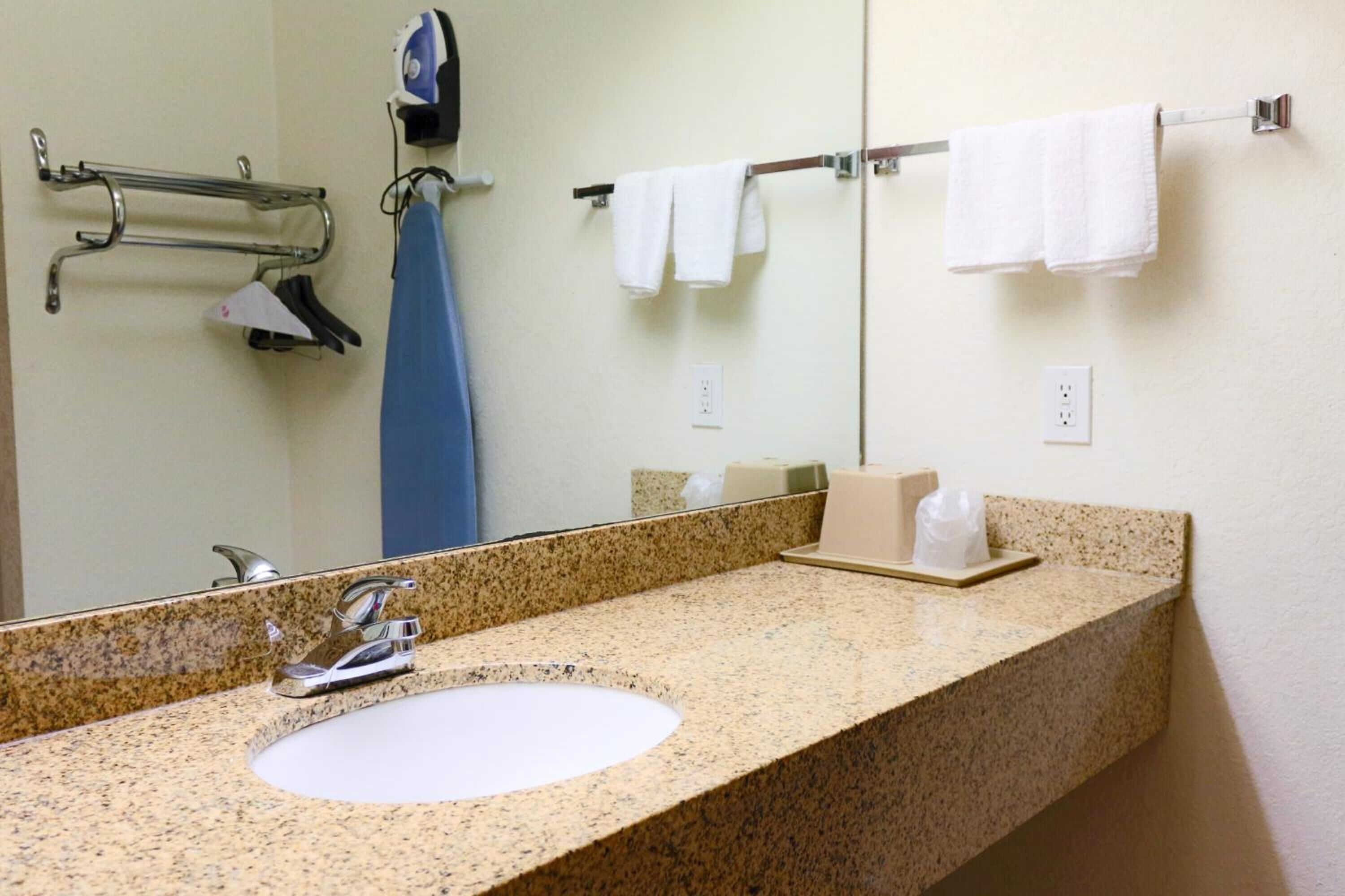 A bathroom with a granite countertop sink, a mirror, a towel rack with white towels, and a soap dispenser.