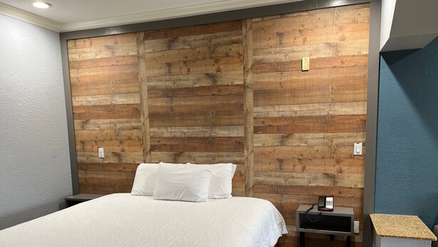 Ein Schlafzimmer mit einem Holzkopfteil, einem Bett mit weißer Bettwäsche, einem Nachttisch mit Telefon und einem kleinen Tisch mit Lampe.